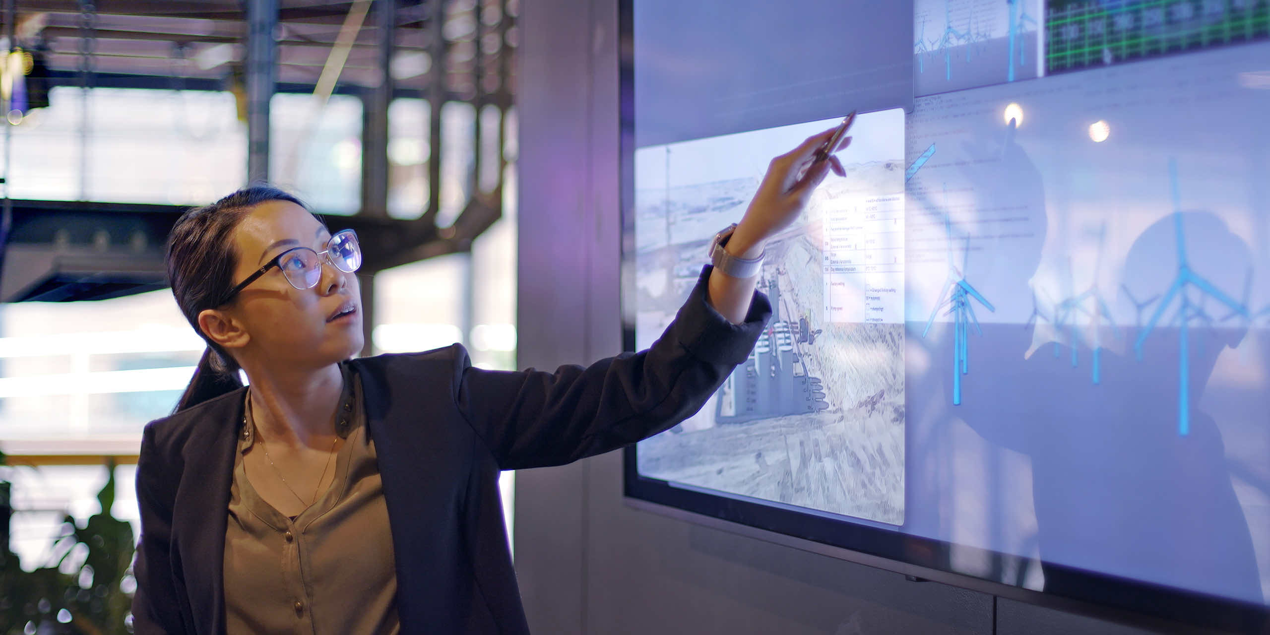 A business associate conducts a meeting with the aid of a large screen displaying solar panels & wind turbines.